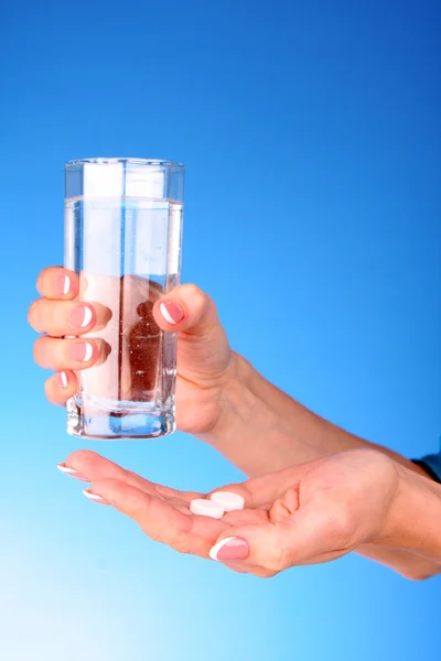 Tabletten en glas water bij de vrouw handen op blauwe achtergrond — Stockfoto