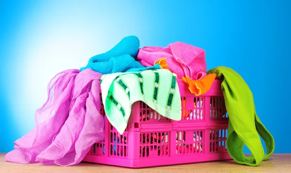 Roupas brilhantes em uma cesta de lavanderia no fundo azul — Fotografia de Stock