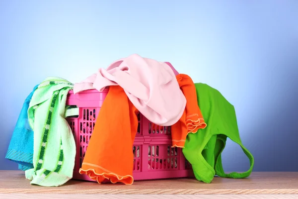Bright clothes in a laundry basket on blue background — Stock Photo, Image