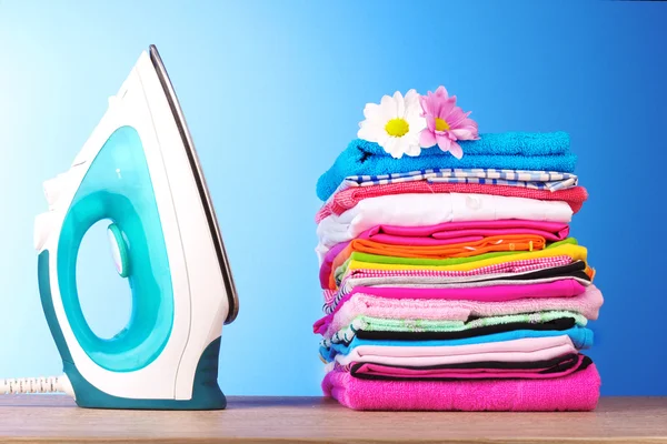 Σωρό από πολύχρωμα ρούχα και ηλεκτρικό σίδερο σε μπλε φόντο — Φωτογραφία Αρχείου