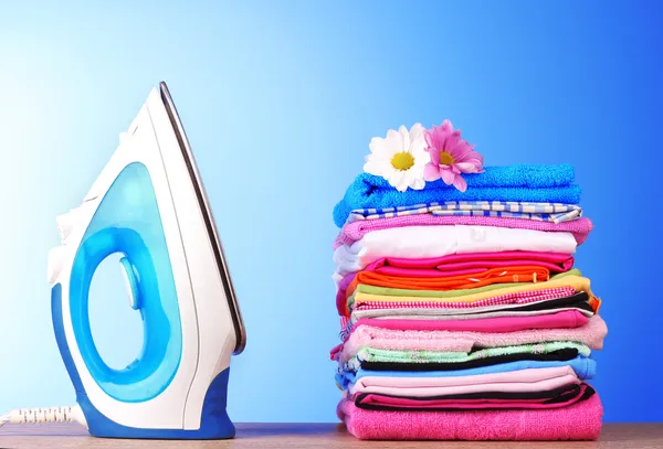 Pile of colorful clothes and electric iron on blue background — Stock Photo, Image