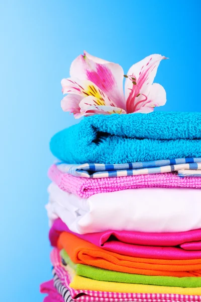 Haufen bunter Kleidung und Blumen auf blauem Hintergrund — Stockfoto