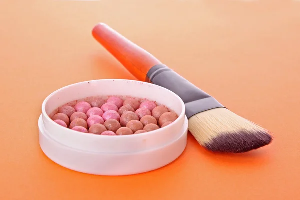 Kosmetikpinsel und Rouge auf orangefarbenem Hintergrund — Stockfoto