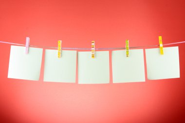 Blank paper sheets on a clothes line against the red background clipart