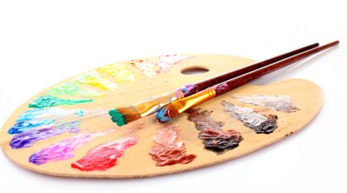 Wooden art palette with blobs of paint and a brush on white back