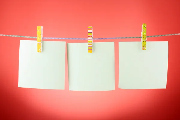 Fogli di carta bianchi su una linea di vestiti sullo sfondo rosso — Foto Stock