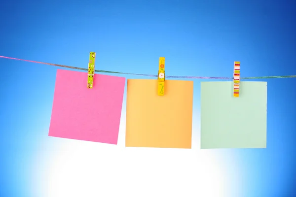 Fogli di carta bianchi su una linea di vestiti su uno sfondo blu — Foto Stock