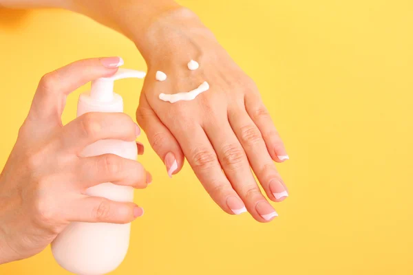 Close-up de belas mãos femininas aplicando creme de mão no amarelo — Fotografia de Stock
