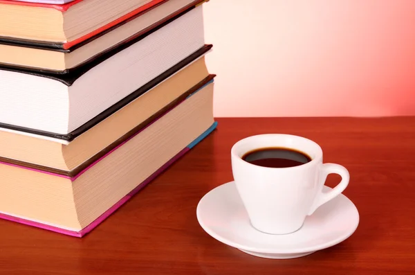 Böcker högen och kopp kaffe på bordet och röd bakgrund — Stockfoto
