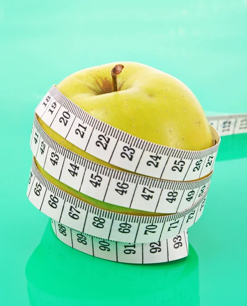 Белая лента измеряется вокруг зеленого яблока, представляющего диету — стоковое фото