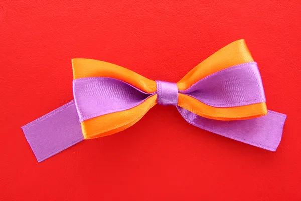 Gift violet and orange bow on red background — Stock Photo, Image