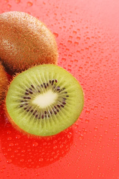 Wet kiwi on red background — Stock Photo, Image