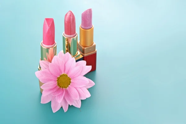 Drei neue Lippenstifte und rosa Blume auf blauem Hintergrund — Stockfoto