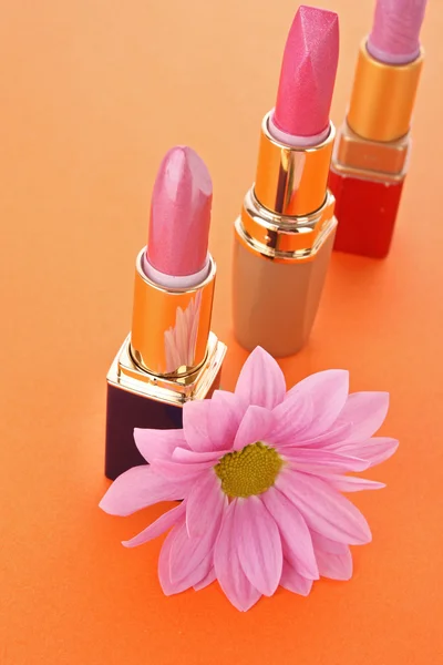 2 つの新しい口紅とオレンジ色の背景にピンクの花 — ストック写真