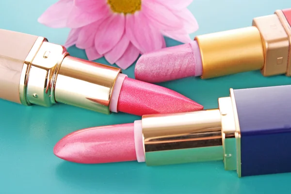 Three new lipsticks and pink flower on blue background — Stock Photo, Image