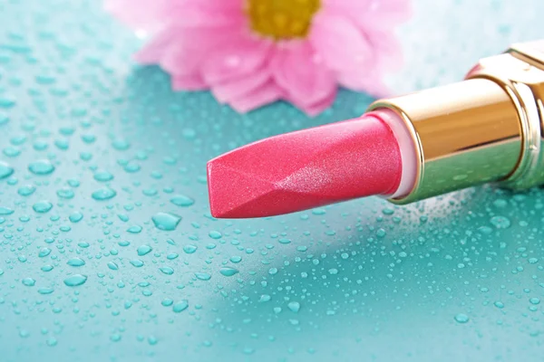 Lippenstift en roze bloem op blauwe achtergrond — Stockfoto