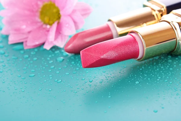Lippenstift en roze bloem op blauwe achtergrond — Stockfoto