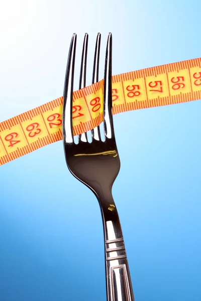 Fork and measuring tape on blue background — Stock Photo, Image