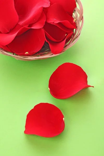 緑の背景に赤いバラの花びらのバスケット — ストック写真