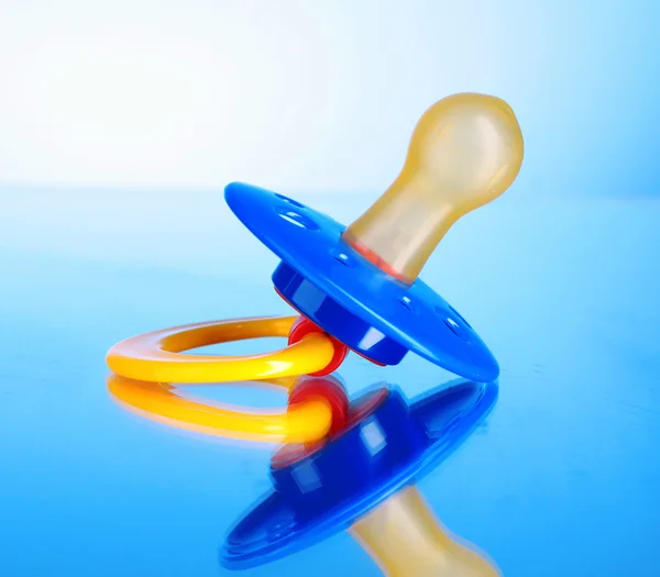 Baby silicone pacifier in blue, red and yellow colors on blue — Stock Photo, Image