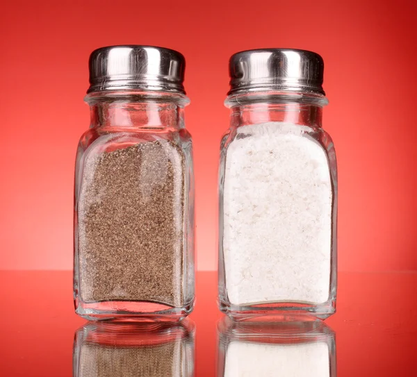 Szkło sól i pieprz shakers na czerwonym tle — Zdjęcie stockowe