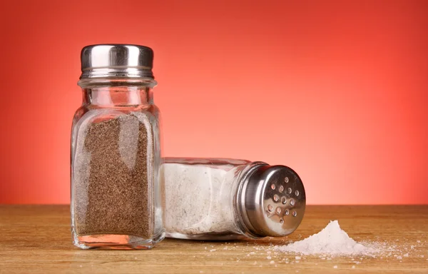 Glas zout en peper shakers op rode achtergrond — Stockfoto