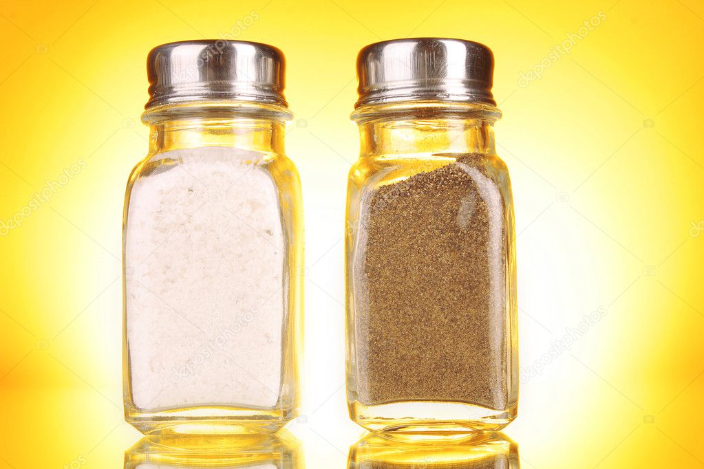 Glass salt and pepper shakers on yellow background