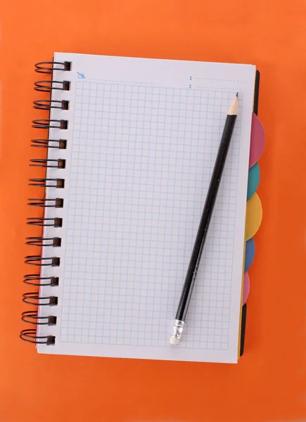 Cuaderno con lápiz sobre fondo naranja — Foto de Stock