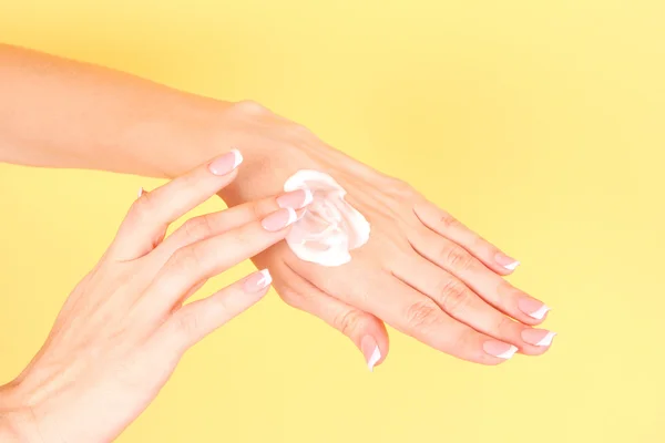 Closeup krásné ženské ruce vyrovnávací krém na ruce na žluté — Stock fotografie