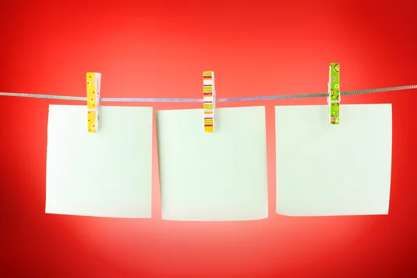 Fogli di carta bianchi su una linea di vestiti sullo sfondo rosso — Foto Stock