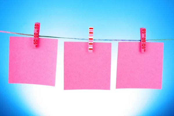 Leere Papierblätter auf einer Wäscheleine auf blauem Hintergrund — Stockfoto