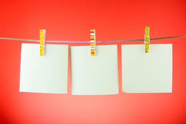 Leere Papierbögen auf einer Wäscheleine vor rotem Hintergrund — Stockfoto