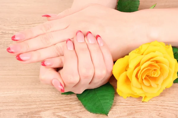 Χέρια γυναίκα με κόκκινο γαλλικό μανικιούρ και κίτρινο λουλούδι — Φωτογραφία Αρχείου