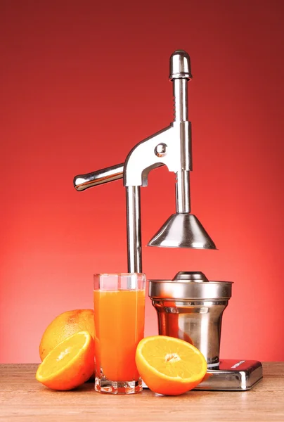 Juicer en sinaasappelen op rode achtergrond — Stockfoto