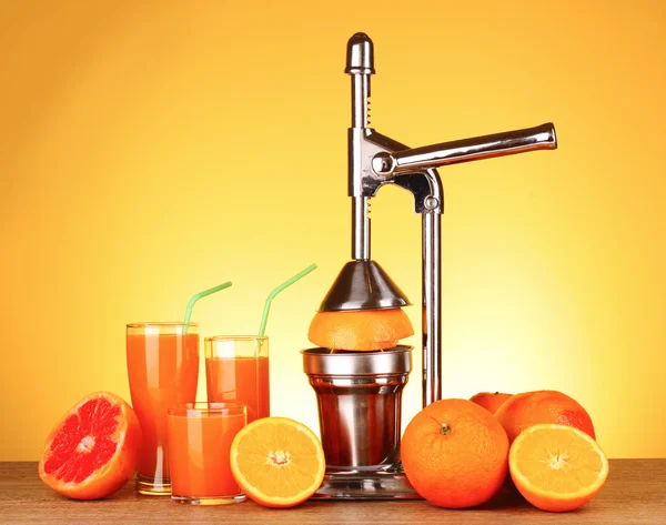 Juicer en sinaasappelen op gele achtergrond — Stockfoto