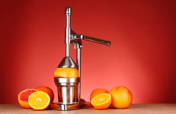 Соковыжималка и апельсины на красном фоне — стоковое фото