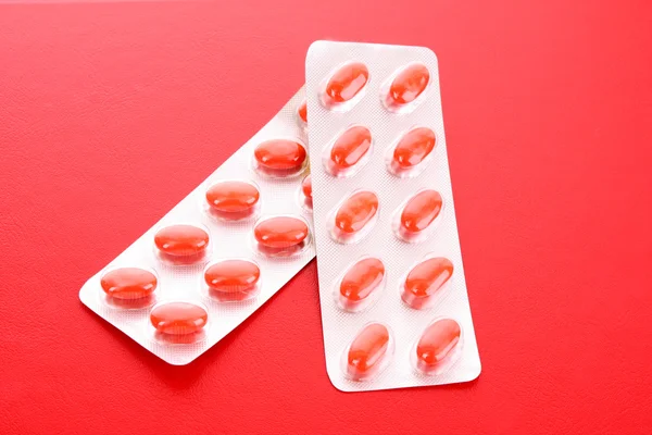 Rote Kapseln mit Vitaminen auf rotem Hintergrund — Stockfoto