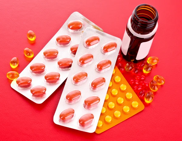 Röda kapslar av vitaminer på en röd bakgrund — Stockfoto