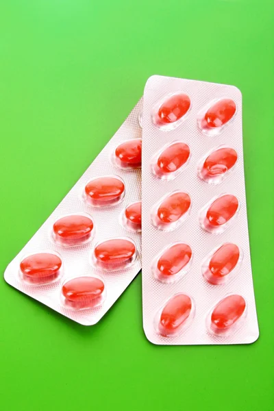 Röda kapslar av vitaminer på en grön bakgrund — Stock fotografie