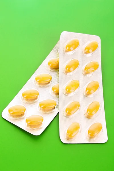 Cápsulas amarillas de vitaminas sobre un fondo verde — Foto de Stock