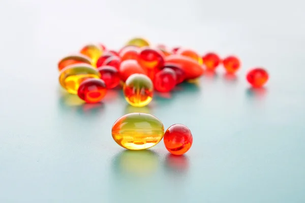 Piros és sárga kapszula vitaminokkal, kék háttérrel — Stock Fotó