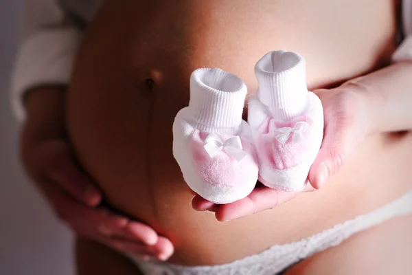 Mulher grávida segurando um par de botas de bebê rosa — Fotografia de Stock