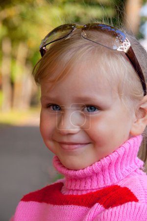 Petite fille blonde souriante portrait gros plan en pull rose 